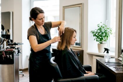 Un parrucchiere sta dando forma ai capelli di una donna, accorciandoli fino alle spalle nel suo salone.