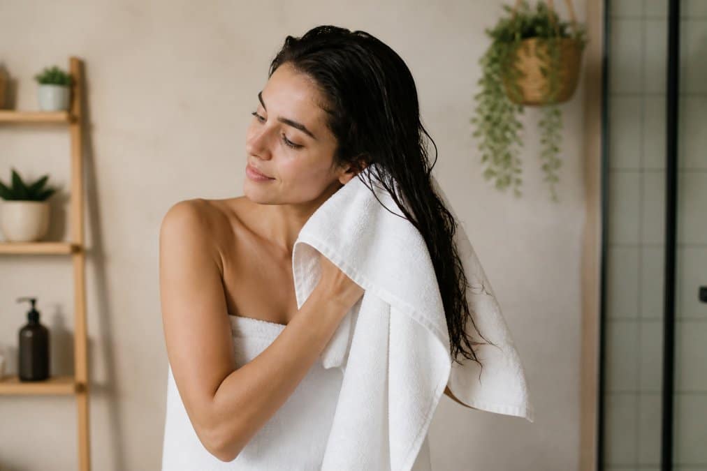 Donna che tampona delicatamente i capelli bagnati con un asciugamano in microfibra, capelli ancora umidi ma non gocciolanti